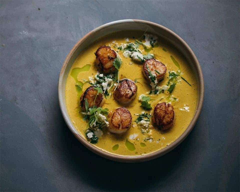Delicious seared scallops in turmeric sauce garnished with cilantro and herbs.