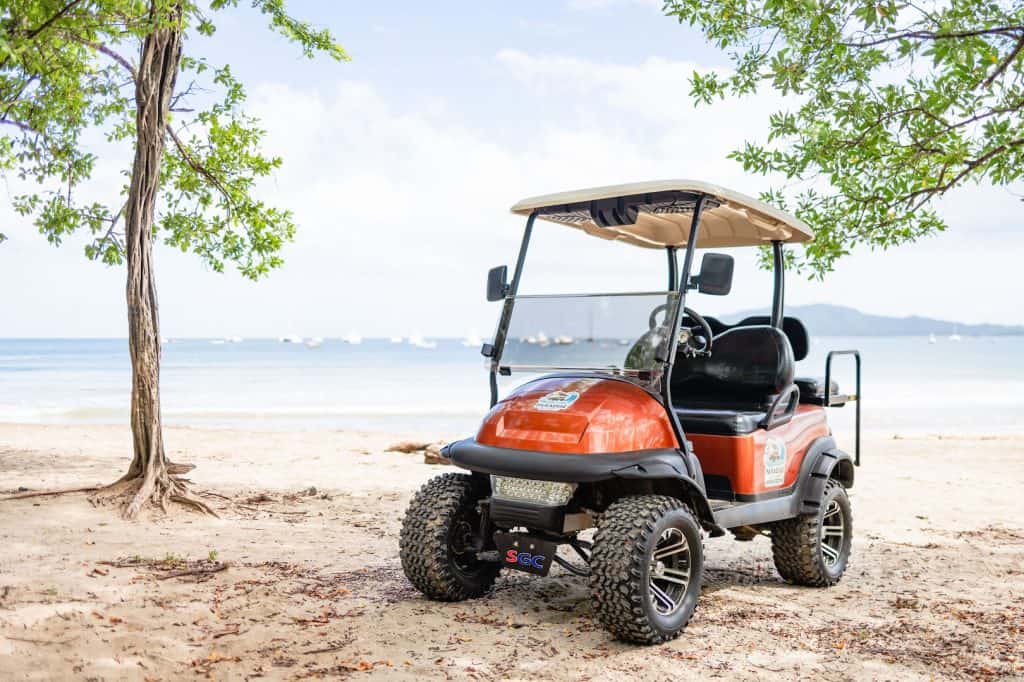 Golf cart on Tamarindo beach with trees and ocean view.