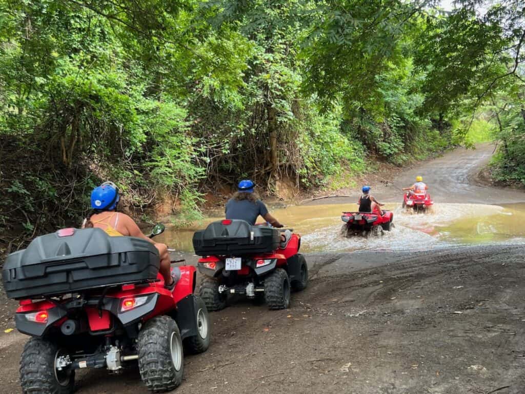 ATV tour riders crossing a shallow river on a forest trail near Tamarindo
