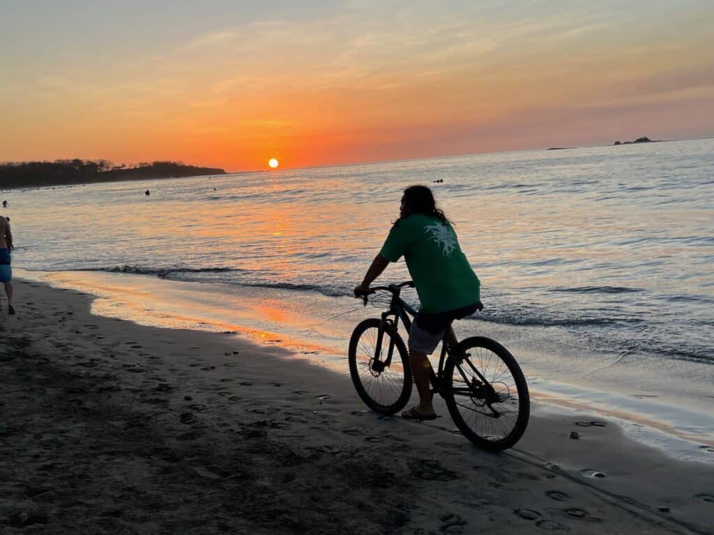 Person riding a bicycle along Tamarindo Beach at sunset