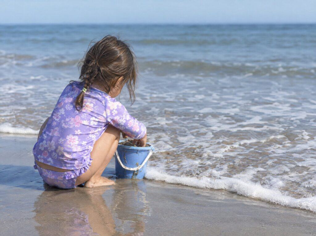 Young child filling a sand bucket at the waterline