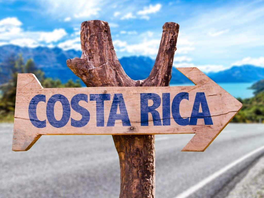 Wooden arrow sign reading Costa Rica beside a paved road