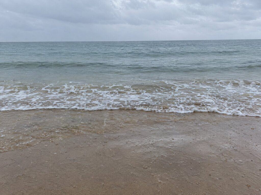 Light rain falling on the beach at the waterline under grey skies