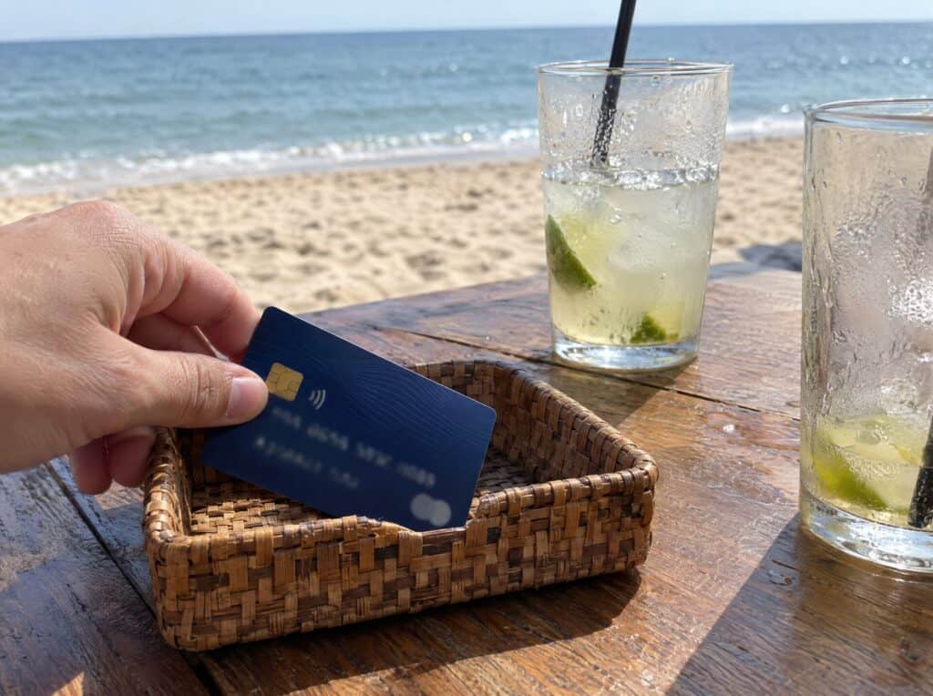 Paying with a card at a beach bar table with drinks and the ocean behind