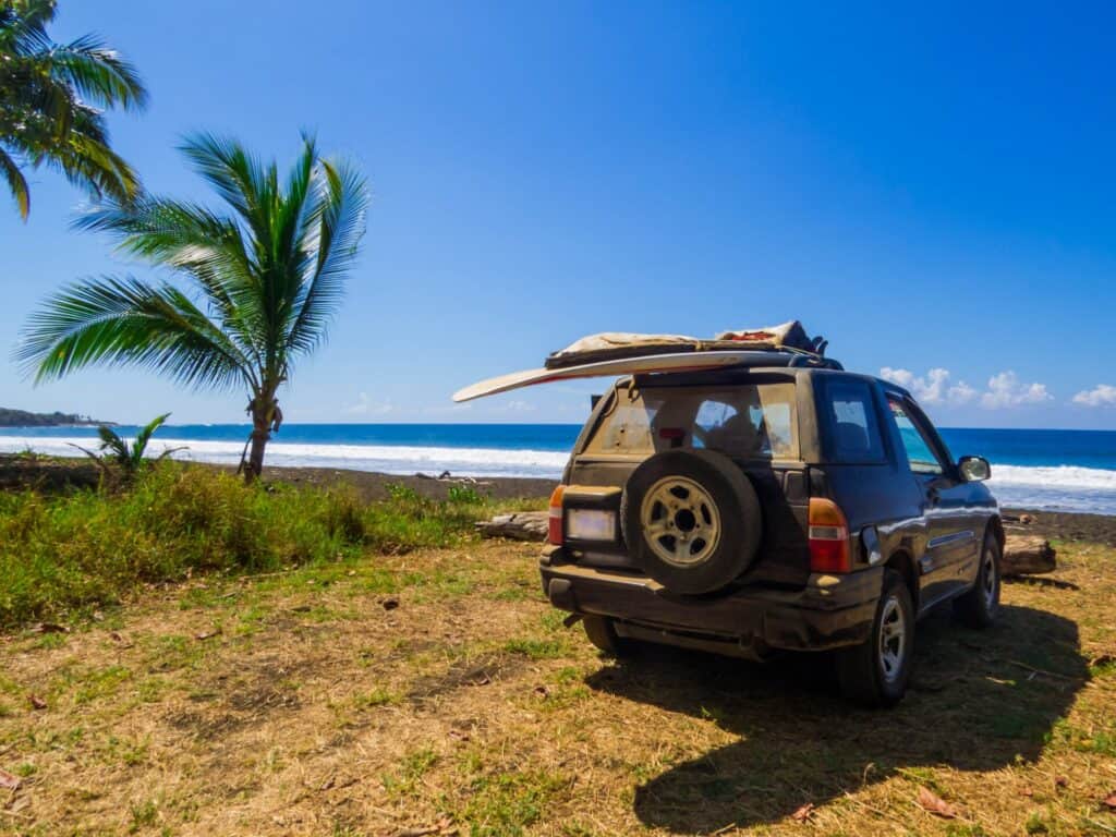 Rental SUV with a surfboard on the roof parked near the beach