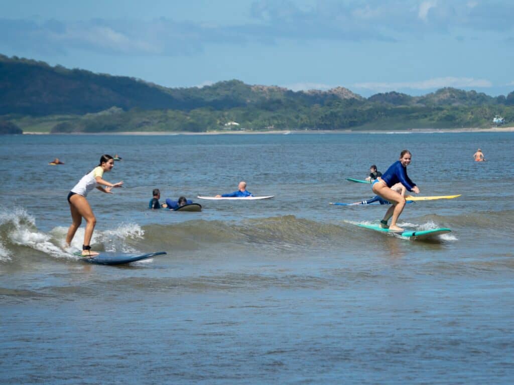 Two surf students standing up on their boards during a lesson in Tamarindo