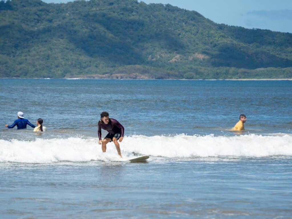 Surfer riding white water near swimmers at Tamarindo Beach