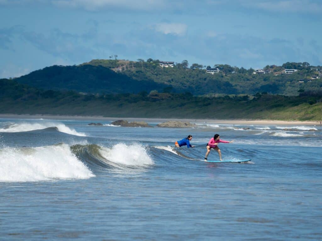 Surfers riding a wave with hillside homes behind