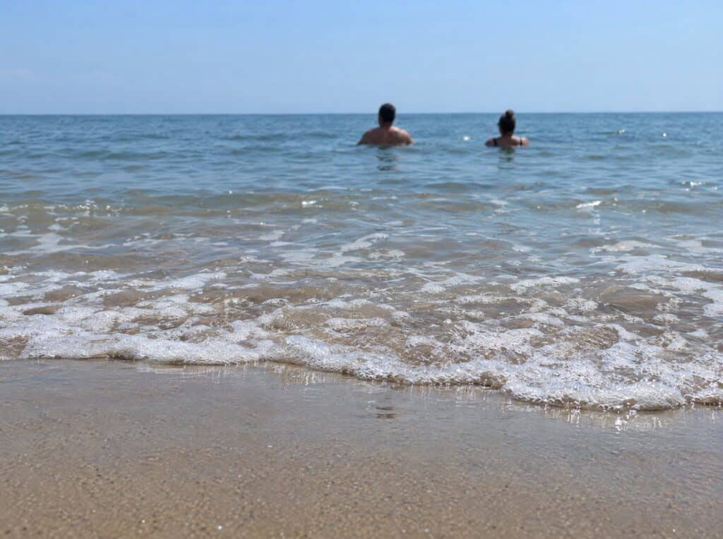 Two swimmers in calm water seen from the shore